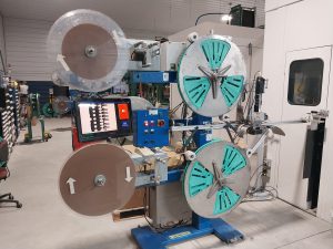 A large industrial machine in a factory setting features multiple spools and a control panel with a screen displaying graphics. Machinists in Central PA might find this equipment essential for manufacturing or stamping tasks.