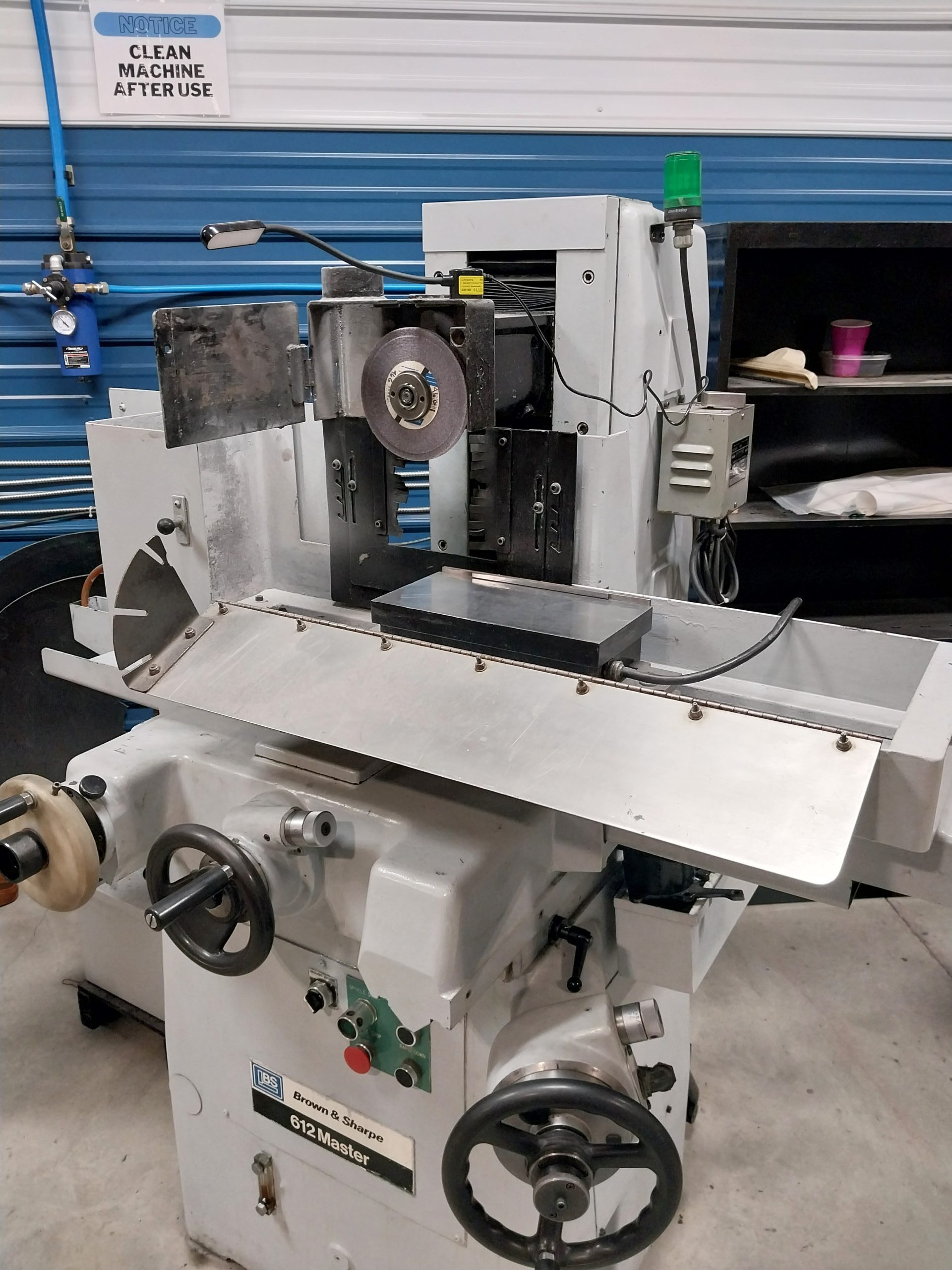 A metalworking machine with a grinding wheel and various controls sits in a workshop backdrop. A sign reads "CLEAN MACHINE AFTER USE," while the blue-striped wall enhances the setting's style. Quality craftsmanship shines here, reflecting Central PA specialists' dedication.