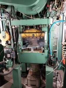 A large industrial machine with various wires and mechanical components is situated in a workshop. Featuring a green exterior, it boasts a transparent section revealing inner workings. It stands on a platform surrounded by quality tools and cables, facilitating precise operations in Central PA's manufacturing scene.