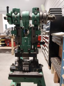 A green industrial metalworking machine stands in a workshop in Central PA. Shelves with tools and equipment are visible in the background. The machine, from Advanced Tooling Solutions, features various bolts, levers, and rotating parts, indicating a complex mechanical function that machinists appreciate.