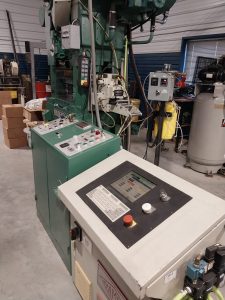 A workshop bustling with industrial machinery features a green metal press ideal for stamping and a control panel with buttons and a screen. Surrounding the equipment are boxes and various electrical components, creating a quality-driven environment tailored for skilled machinists.