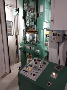 A green industrial stamping press machine with various buttons and controls is prominently labeled "Bruderer." Next to it, a control panel features multiple colored buttons and switches, catering to machinists seeking Advanced Tooling Solutions.