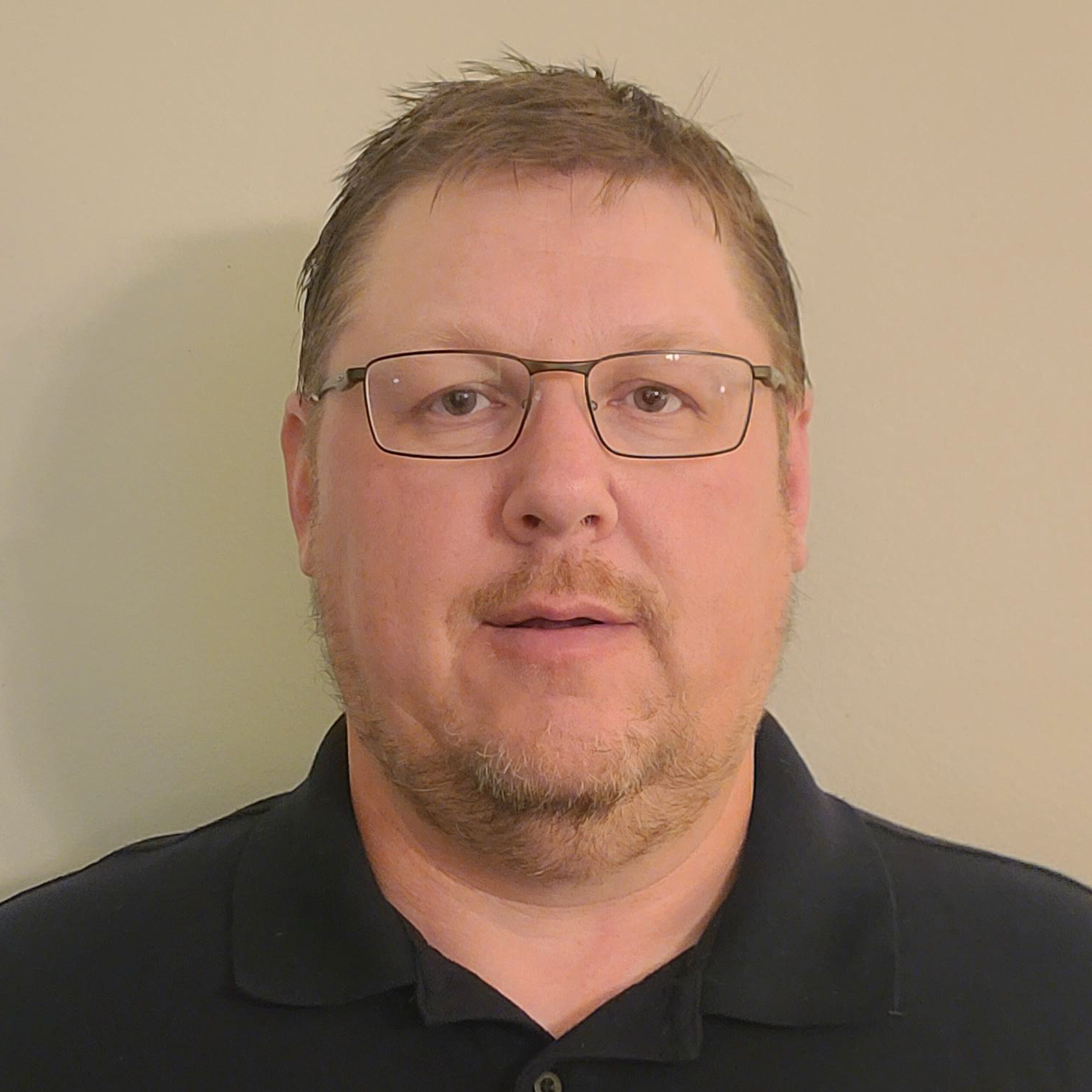 A Central PA machinist with short hair and glasses stands against a plain background, wearing a dark polo shirt.